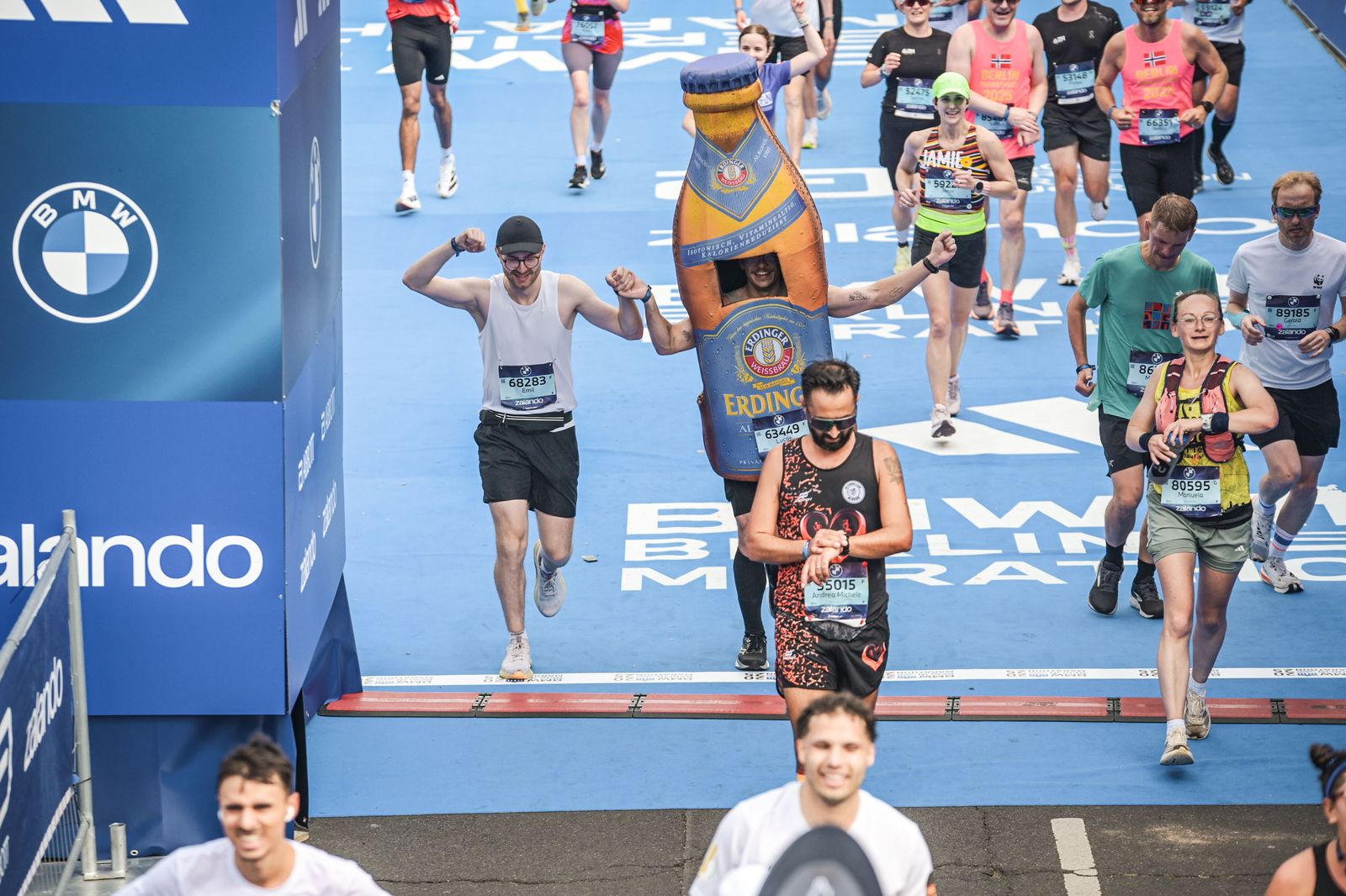 Lucas läuft im Bierflaschen-Kostüm über die Ziellinie des Berlin-Marathons, daneben ein Läufer mit erhobenen Armen