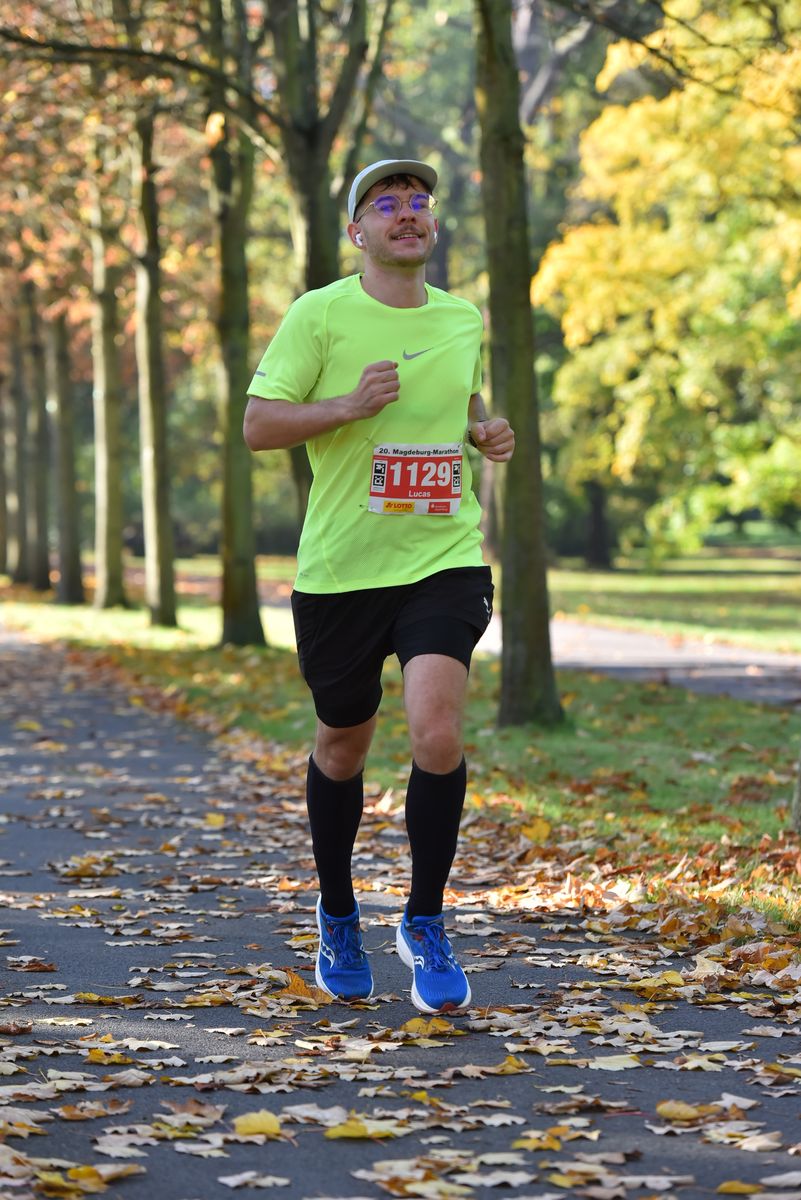 Lucas läuft im neongelben Shirt mit der Startnummer 1129 über einen herbstlichen Parkweg voller Laub
