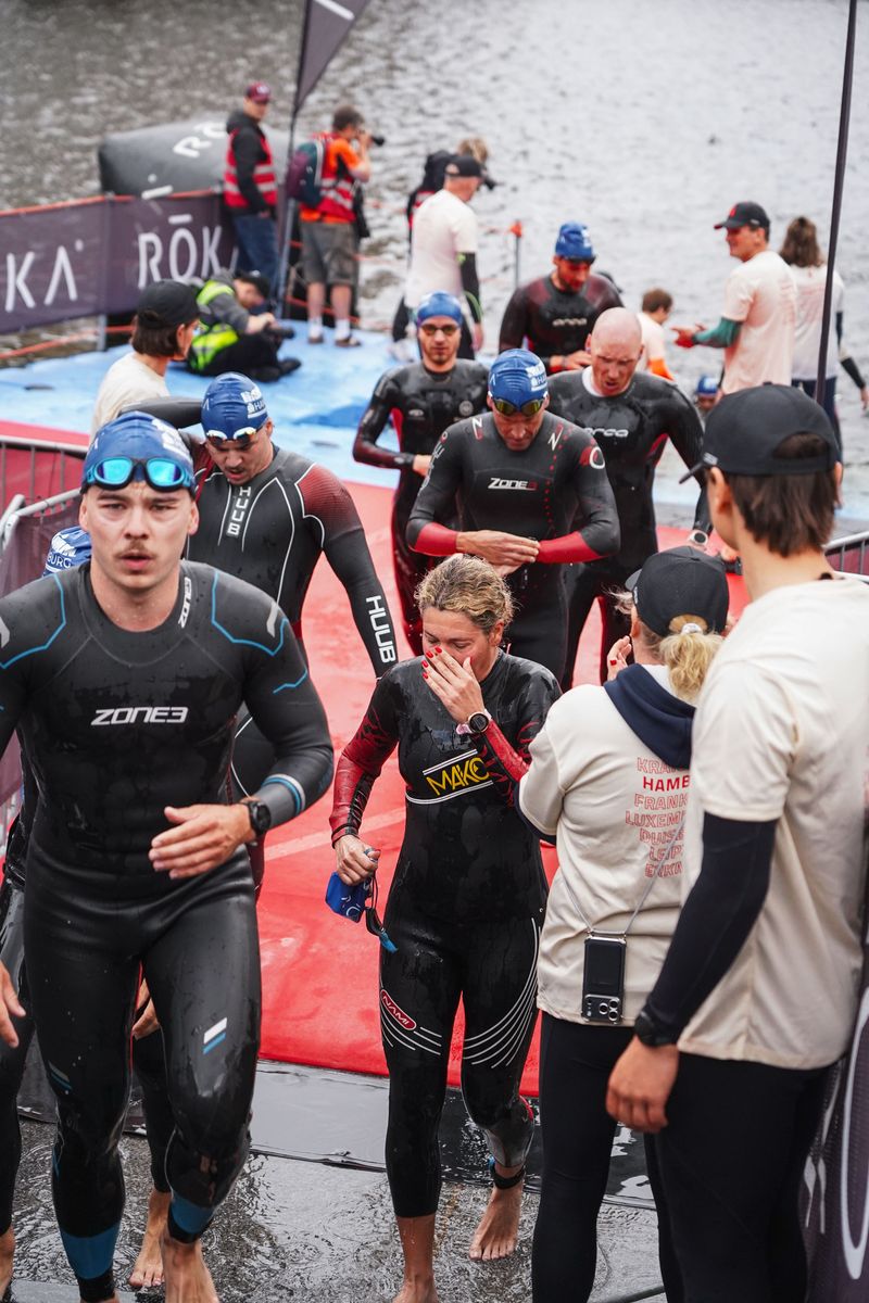 Eine Gruppe Triathletinnen und Triathleten in Neoprenanzügen steigt über eine Rampe aus dem Wasser